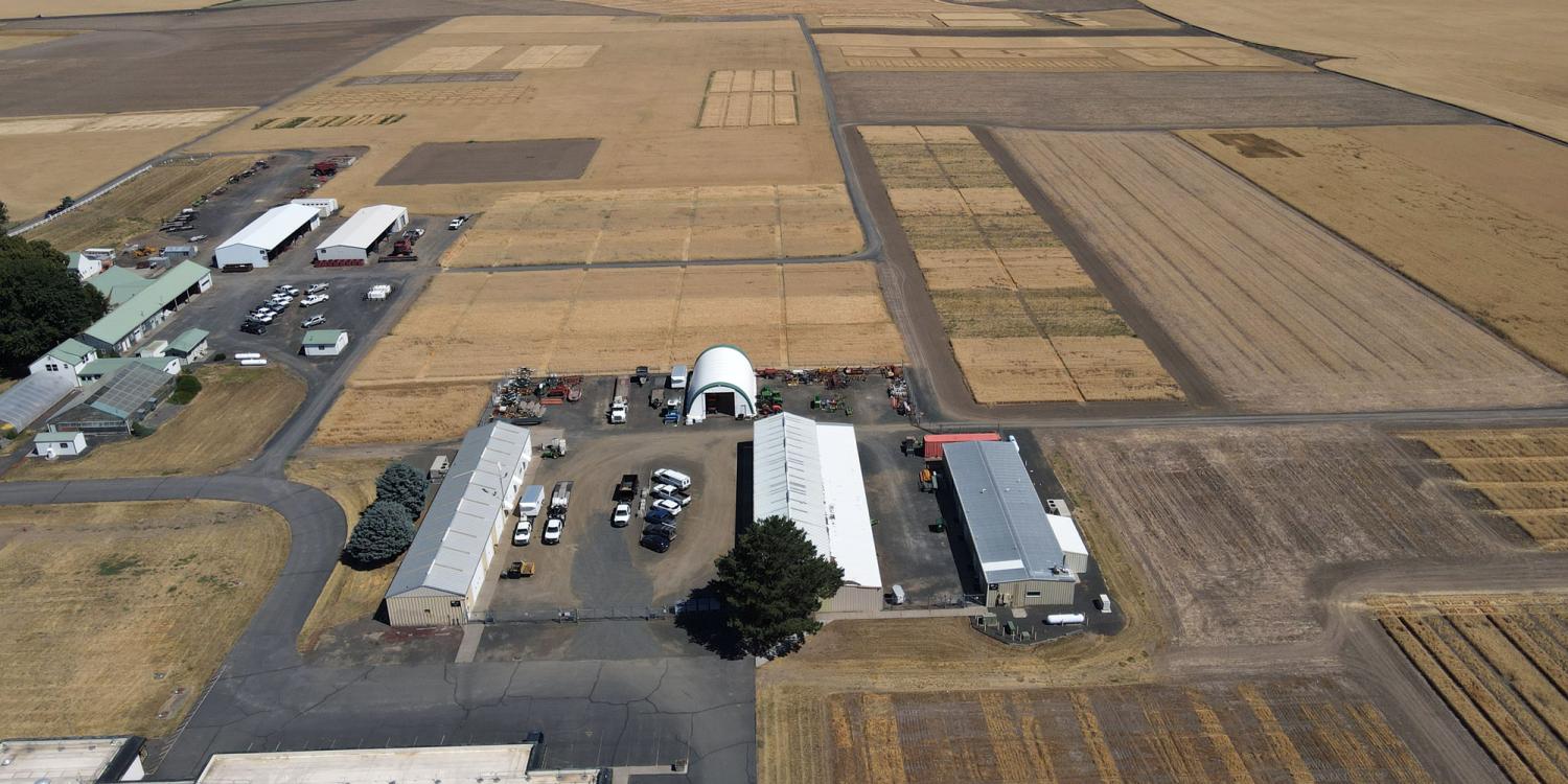 Aerial view of agricultural research station buildings surrounded by large dryland crop plots arranged in rectangular fields across an open landscape.