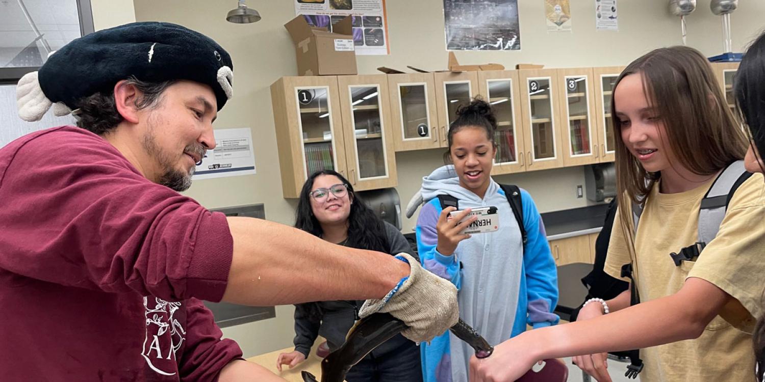 A man holds a Pacific lamprey, an eel-like fish, as it touches the hand of a female student at a middle school.