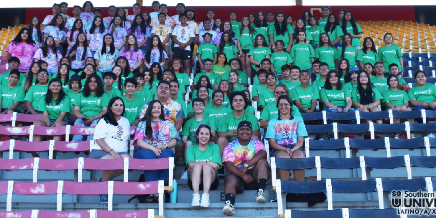 Latinx teenagers and college students pose for a group photo while sitting in seats at a football stadium.