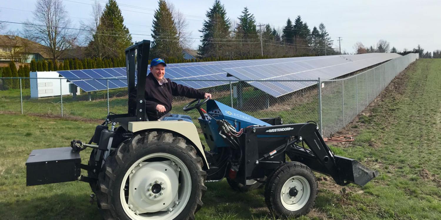 Chad Higgins drives a tractor in front of solar panels installed at the North Willamette Research and Extension Center.
