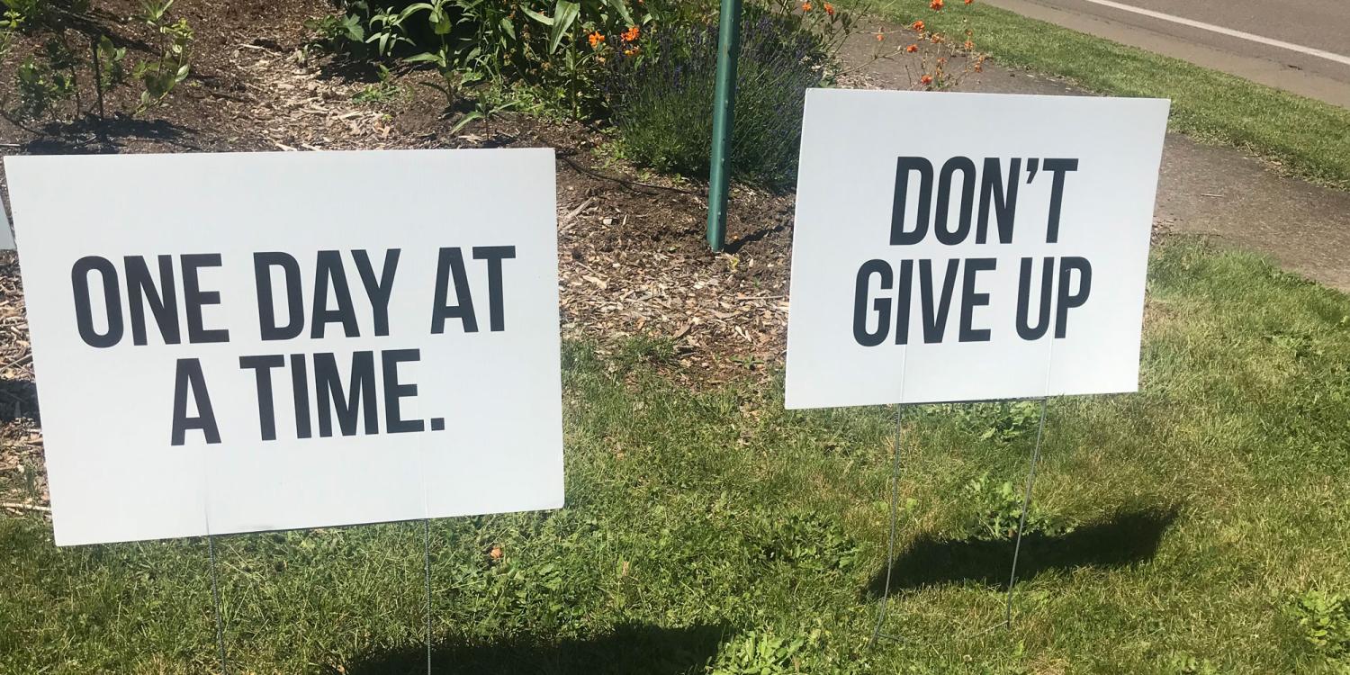 Yard signs that say "One Day at a Time" and "Don't Give Up"