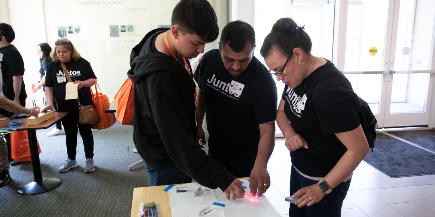 A teenage boy and two adults are using glass to create a prism.