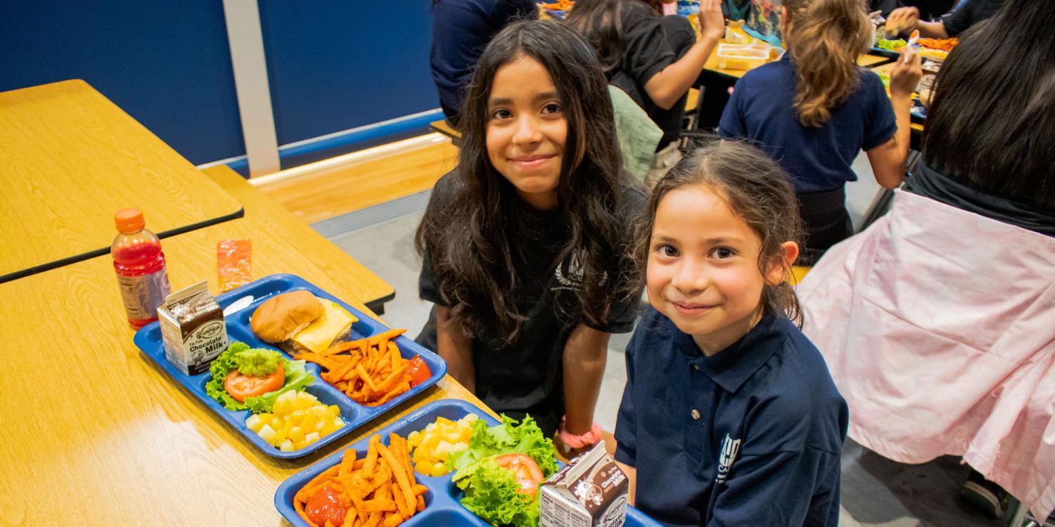 Two girls smile as they get ready to eat a school lunch at Kids Ulimited Academy charter school.