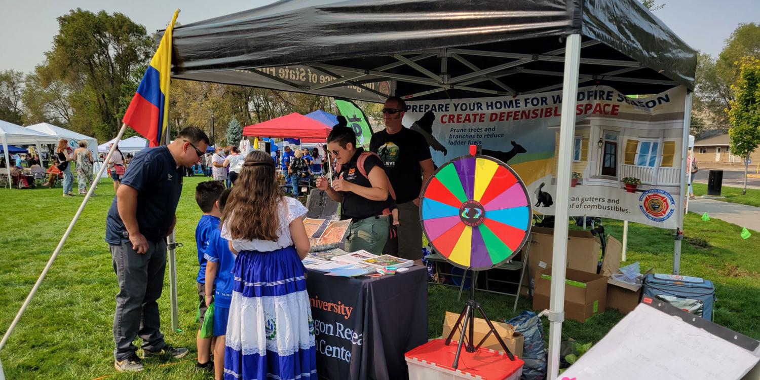 Two children and an adult are visiting an Oregon State University Extension booth at an outdoor festival.