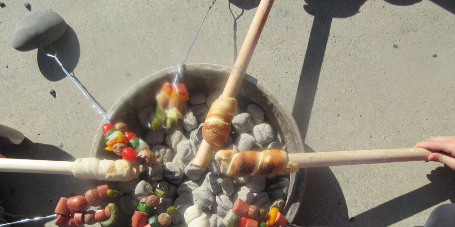 An overview view of skewers with meat and vegetables cooking on a barbecue.