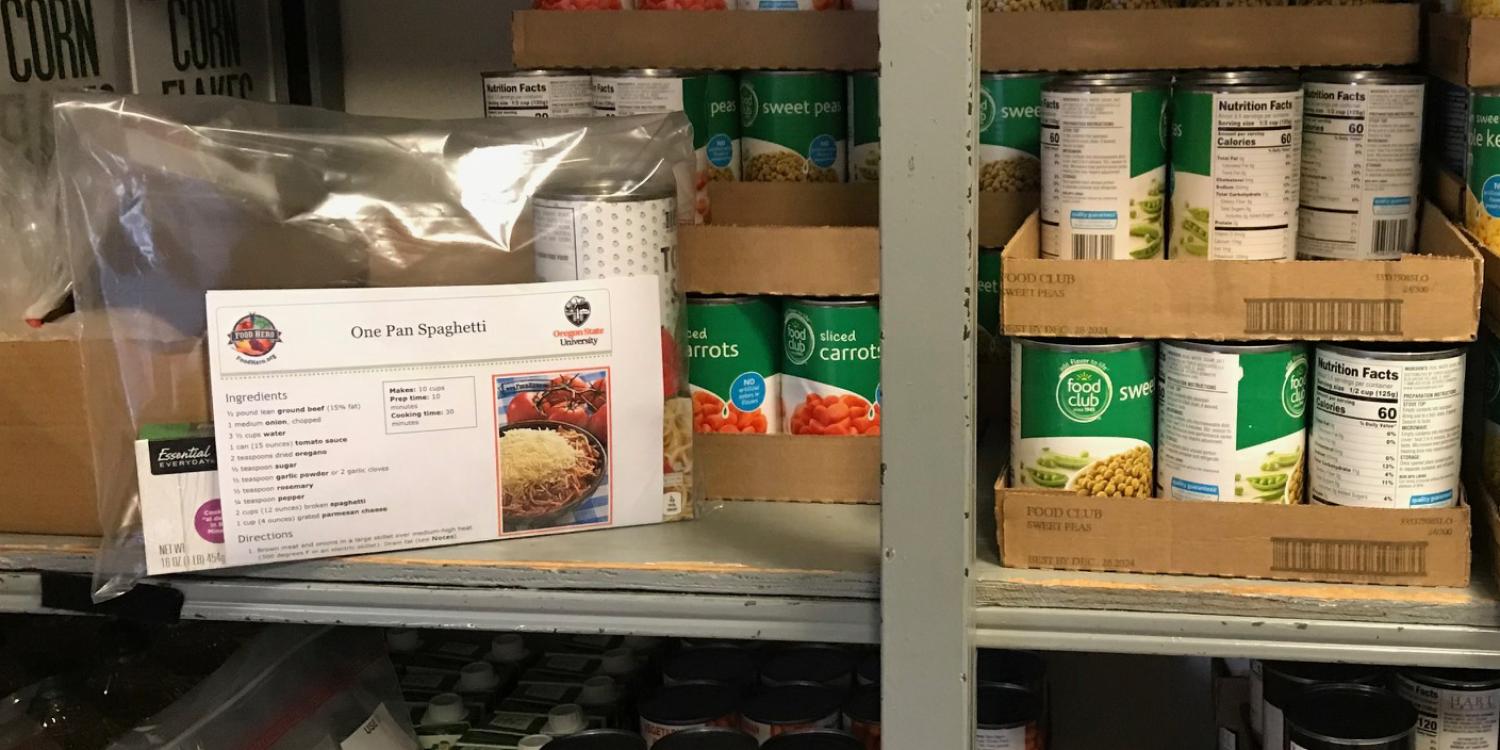 A meal kit sits on a shelf among canned food in a food pantry.