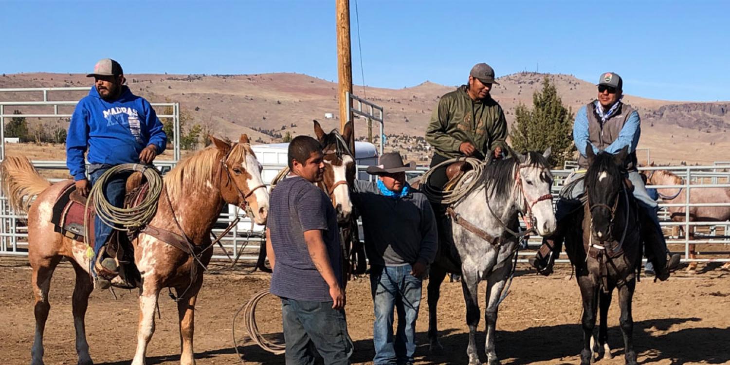 A group of men on horseback and on foot gather in a corral under clear blue skies in Warm Springs.