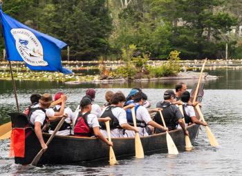 Indigenous students paddle a canoe on Munsel Lake to visit an area that is culturally significant to the Confederated Tribes of Coos, Lower Umpqua and Siuslaw Indians.