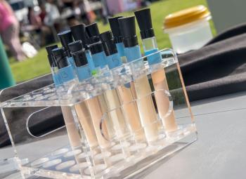 A set of labeled test tubes filled with water samples sits in a clear plastic rack on a table at an outdoor water testing event.