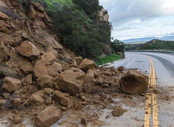 Rocks and dirt from a landslide cover one lane of a two-lane road.