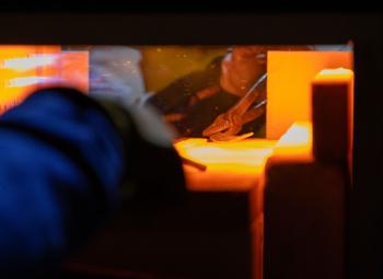 A person uses tongs to place metal inside a glowing forge, preparing it for blacksmithing.