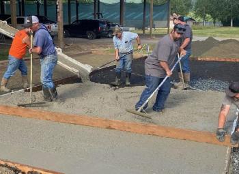 Workers in boots and gloves smooth and level freshly poured cement at a fairground construction site.