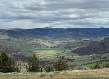 Rolling hills and a green valley stretch across the landscape under a sky filled with layered gray clouds.