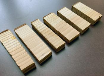 Six rectangular Douglas-fir wood samples arranged in a row on a gray surface, each showing different grain patterns and saw cuts.