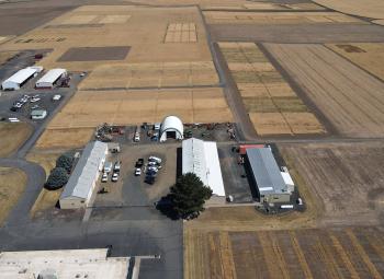 Aerial view of agricultural research station buildings surrounded by large dryland crop plots arranged in rectangular fields across an open landscape.