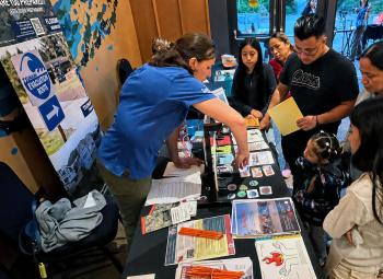 Community members gather around an information table about tsunami evacuation routes and emergency preparedness during a multilingual resource fair.