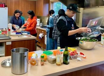 Teens work together in a kitchen preparing food, surrounded by ingredients and cooking supplies on the counter.