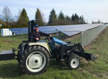 Chad Higgins drives a tractor in front of solar panels installed at the North Willamette Research and Extension Center.