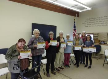 A group of adults stand indoors holding certificates at a graduation event for the Eat Smart, Live Strong program.