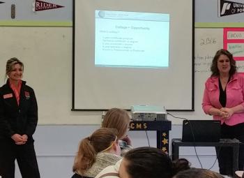 Two women are giving a presentation in front of a middle school class.