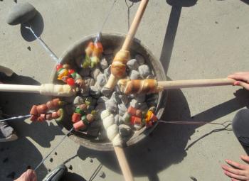 An overview view of skewers with meat and vegetables cooking on a barbecue.