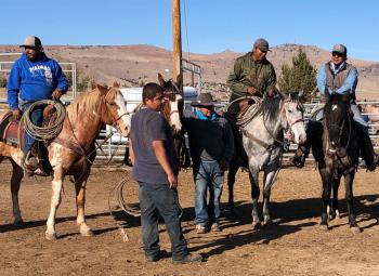A group of men on horseback and on foot gather in a corral under clear blue skies in Warm Springs.
